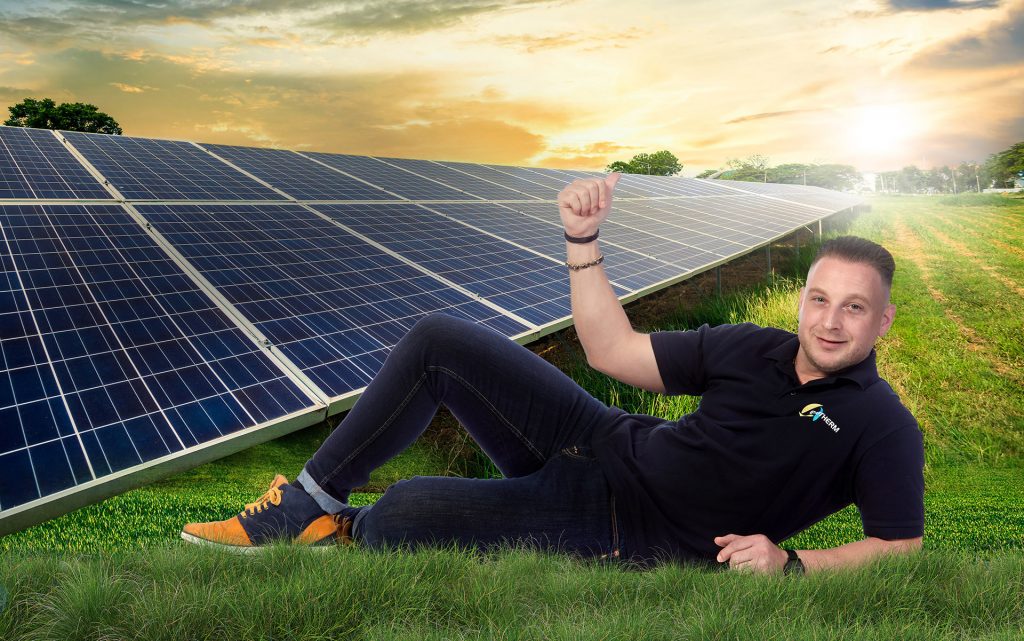 Brice Thomas allongé dans l'herbe en montrant les panneaux solaires Evotherm installés derrière lui